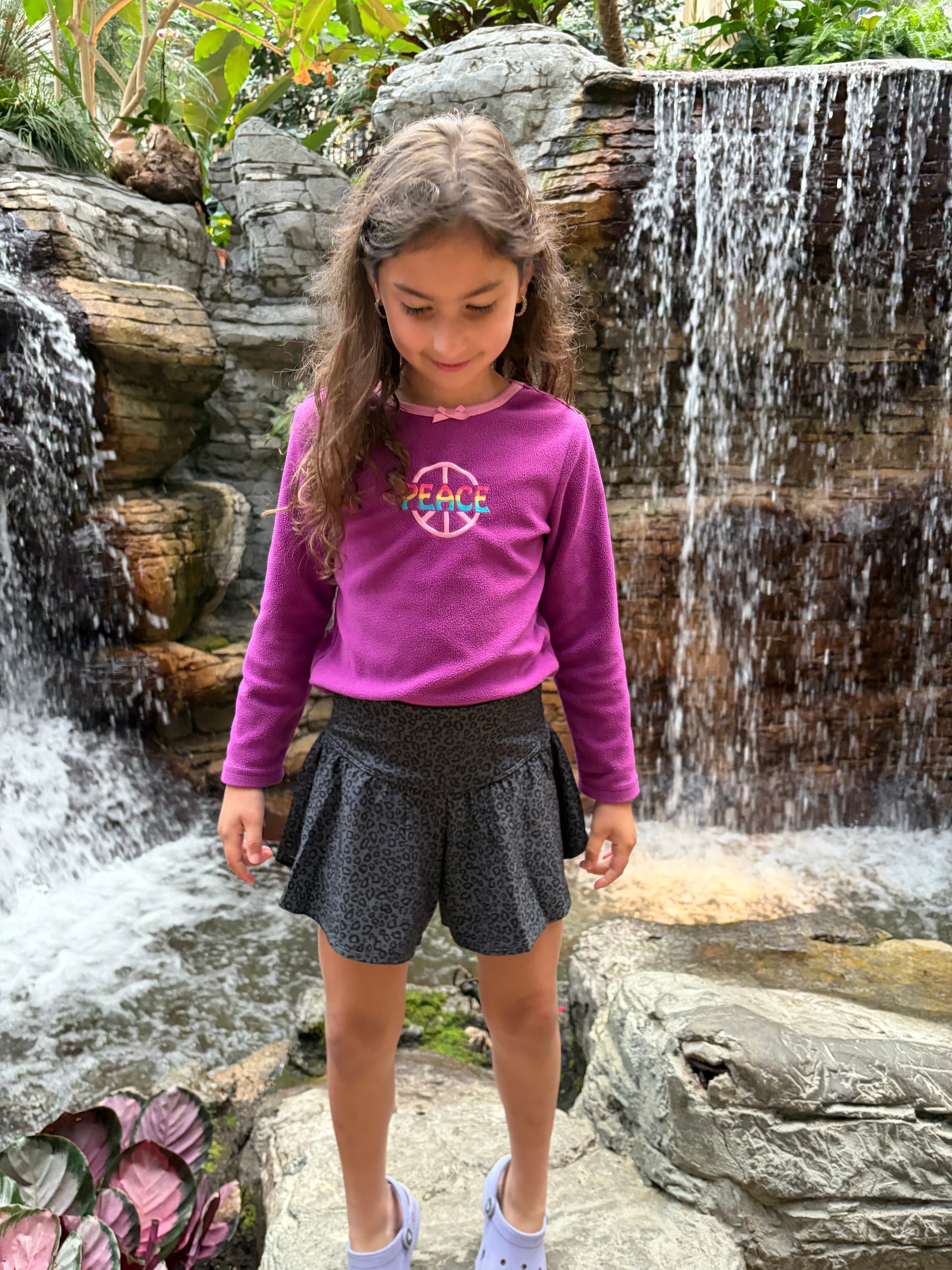 Vanessa in a magenta peace sweater standing by a waterfall